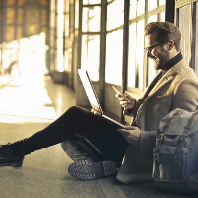 Working man sitting on the floor with a laptop and a smartphone as a symbol for optimal audience reach Working man sitting on the floor with a laptop and a smartphone as a symbol for optimal audience reach